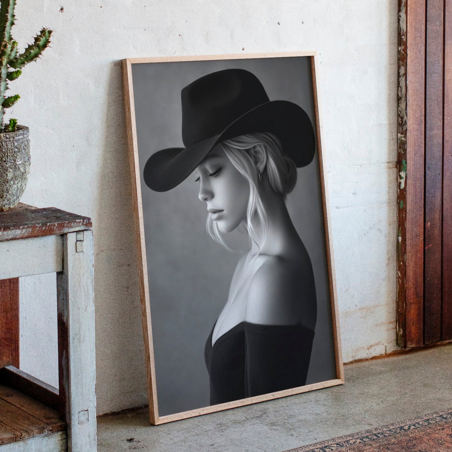 Framed portrait of a woman wearing a cowboy hat next to a potted cactus on a wooden shelf.