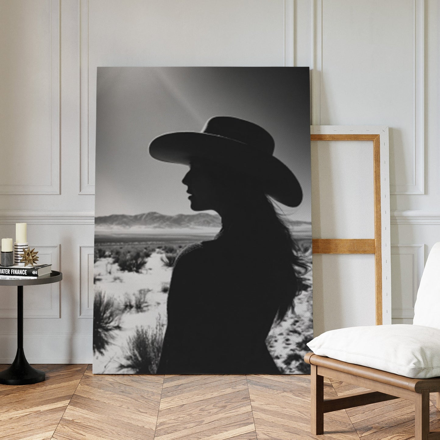 Silhouette of a person wearing a hat in a desert landscape, displayed on a wall in a room with wooden flooring and a chair.