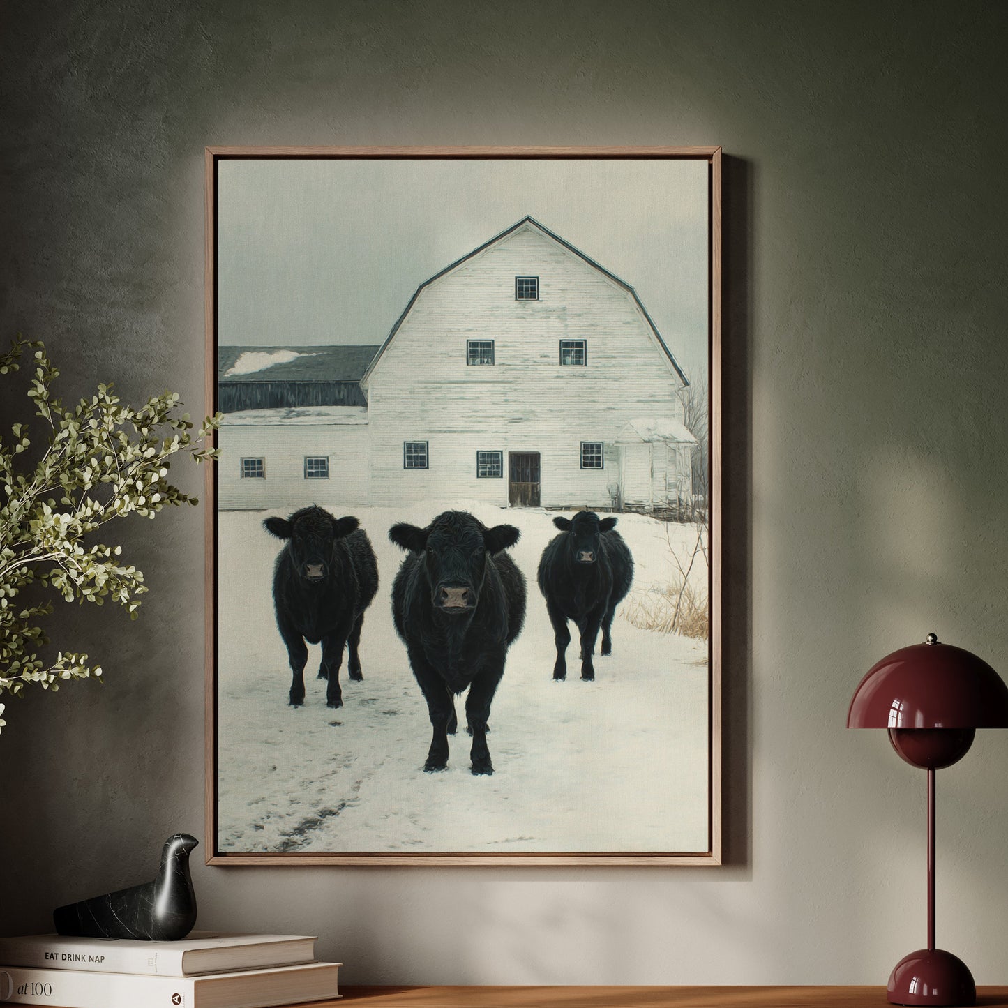 Framed artwork of three black cows in a snowy field on a wall above a wooden console table.