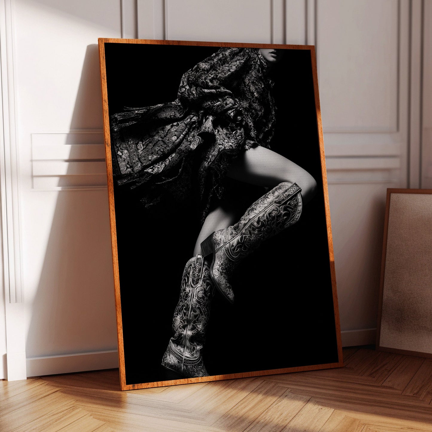 Framed black and white artwork of a person in a chair on a wooden floor.