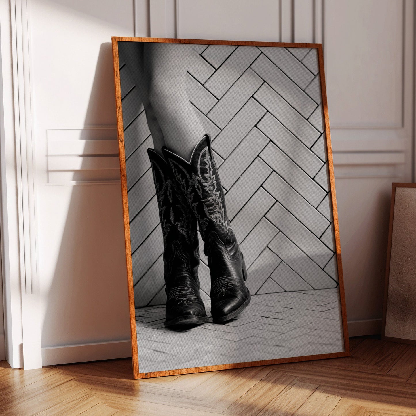 Framed artwork of a person wearing cowboy boots on a chevron-patterned background, leaning against a wall.