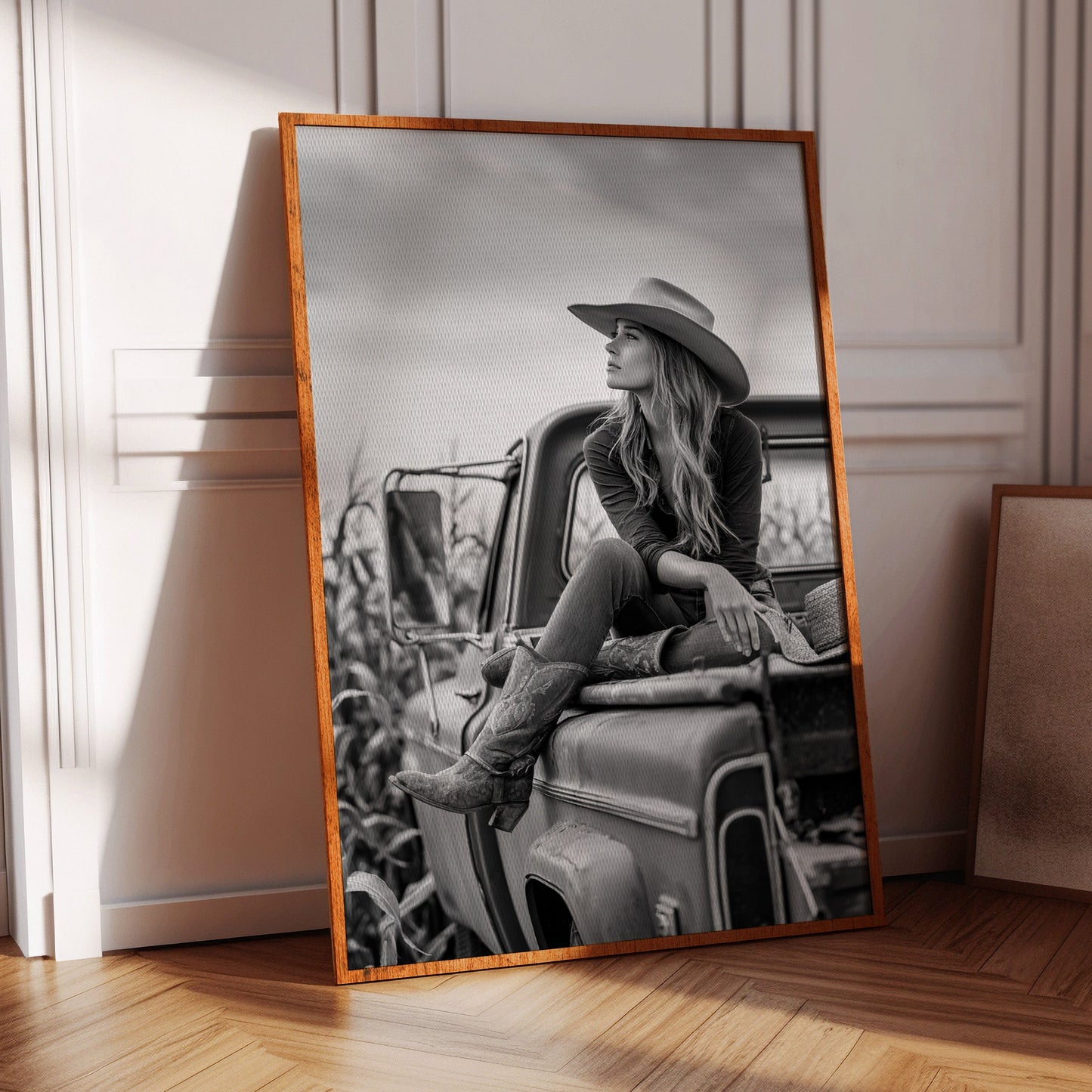 Framed black and white photograph of a woman sitting on a truck in a room with wooden floor and chair.
