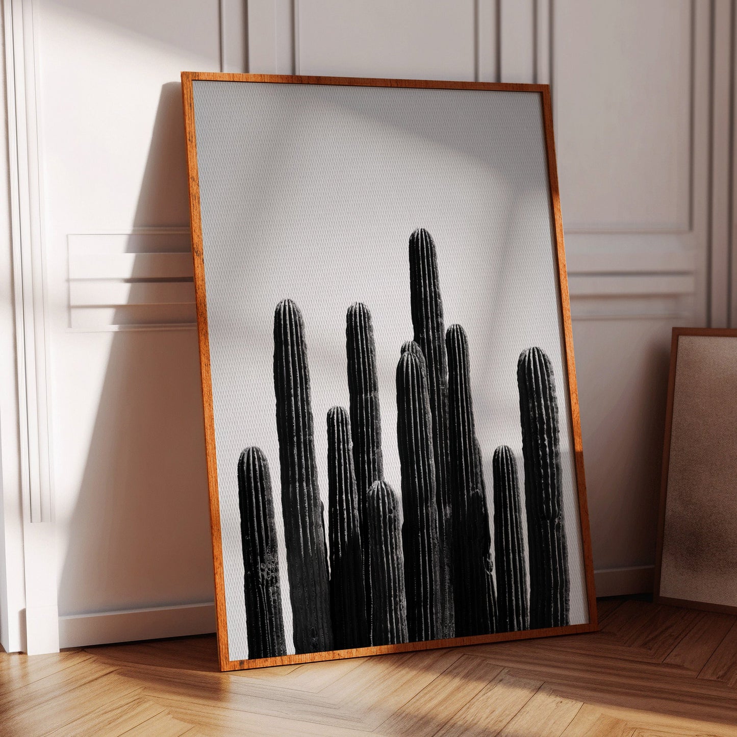 Framed black and white cactus print on a wall in a room with wooden floor and chair.