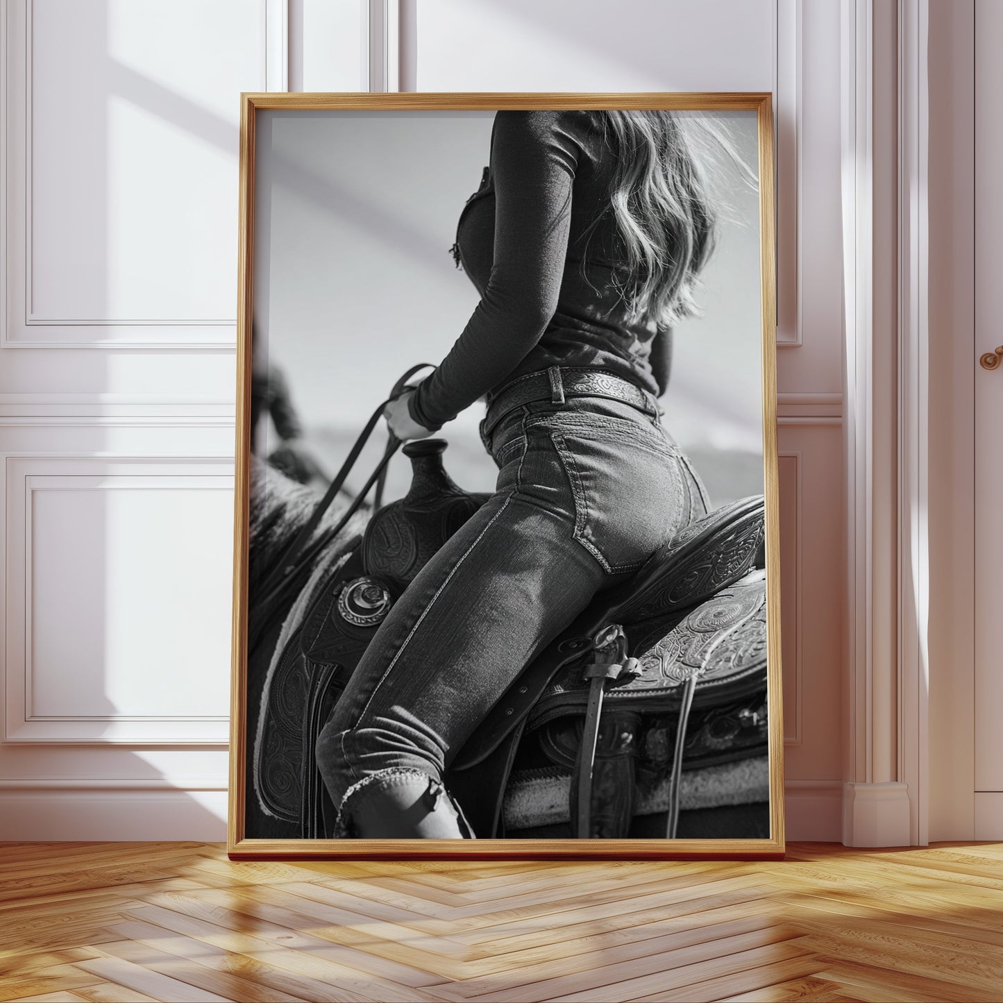 Framed black and white artwork of a person on horseback in a room with wooden floor and white walls.