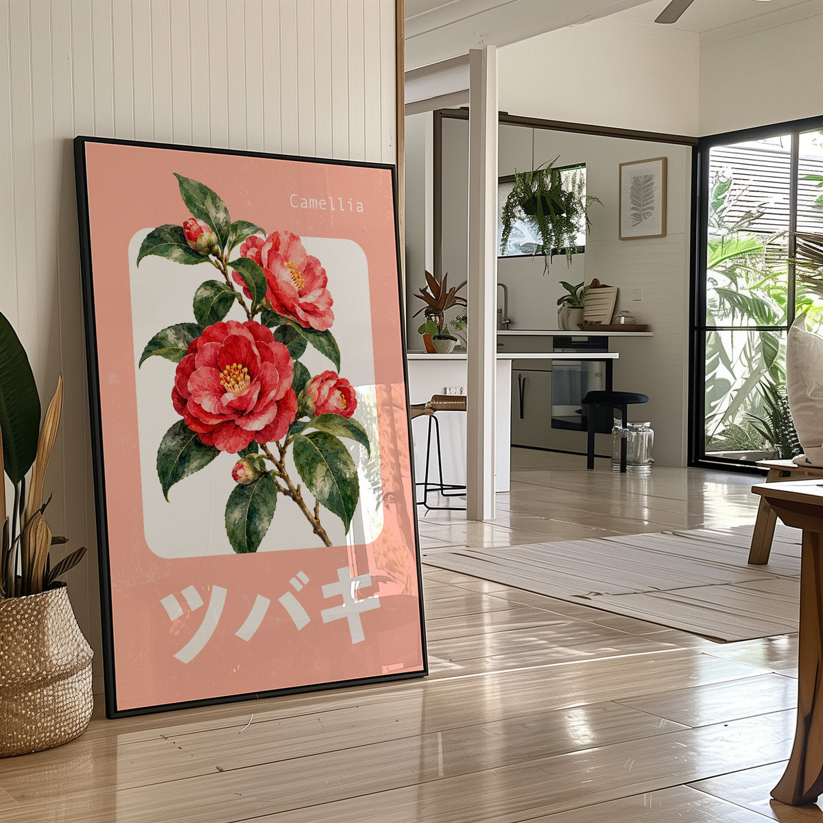 A Camellia Before Noon, a red camellia bloom with green leaves on a blush pink ground, with a rounded cream label and bold pale Japanese lettering, in a flat Japanese travel poster style painted in red, blush pink and cream, in a black frame leaning on a bright hallway floor beside a potted plant