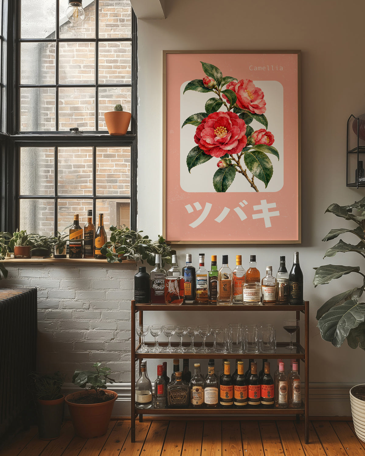 A Camellia Before Noon, a red camellia bloom with green leaves on a blush pink ground, with a rounded cream label and bold pale Japanese lettering, in a flat Japanese travel poster style painted in red, blush pink and cream, in a wood frame on a brick wall above a bar cart of bottles and plants