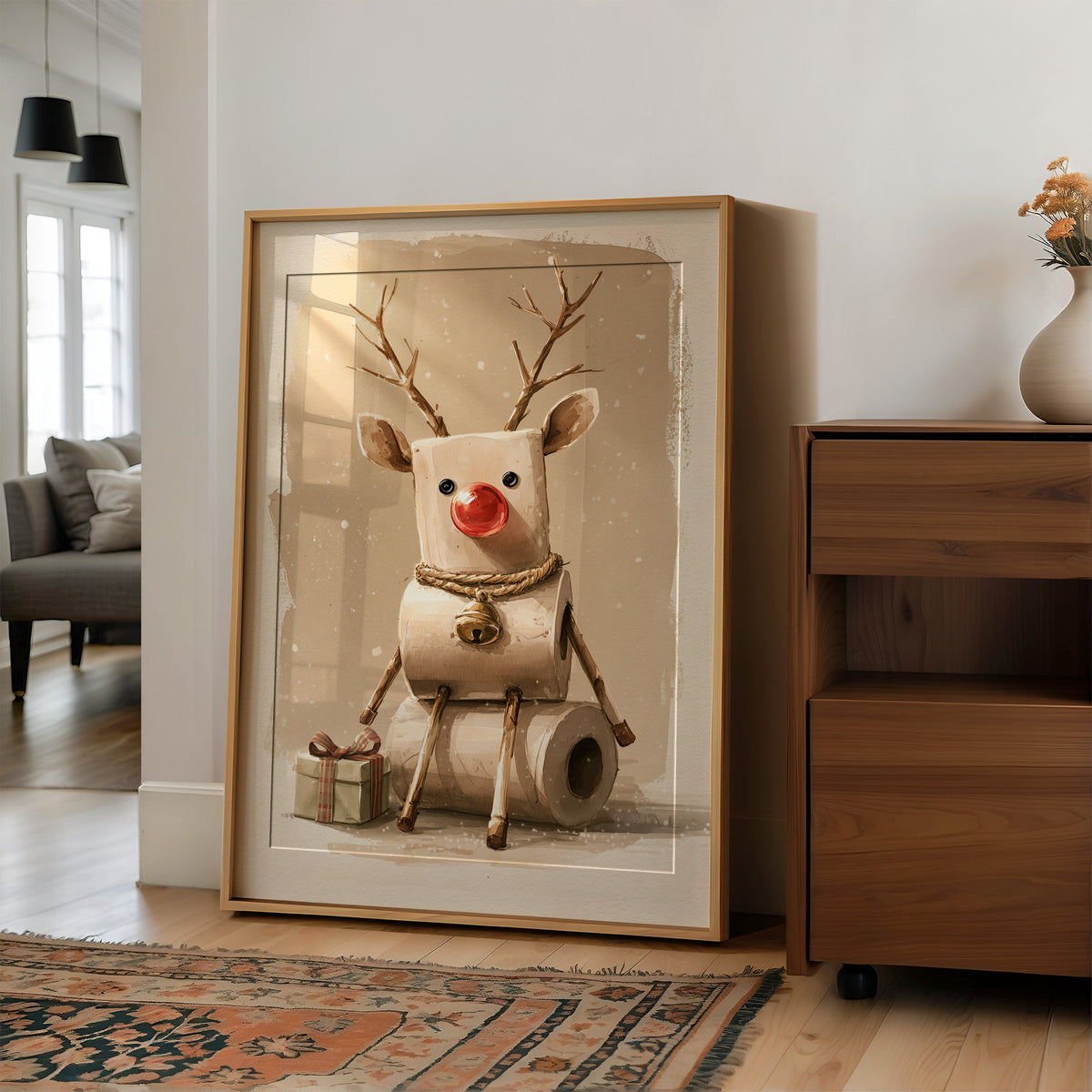 A Reindeer Takes a Seat, a cream reindeer with a red nose and small antlers seated on a stack of rolled tissue, with wrapped gift boxes at its feet, painted in cream, tan and soft red, in a wood frame on a wall beside a walnut cabinet and an open doorway