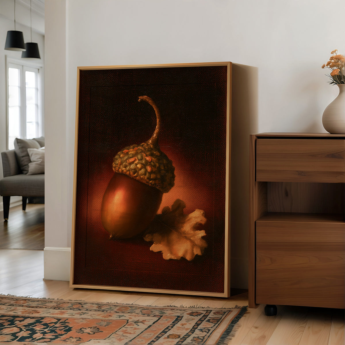 A Single Acorn in Candlelight, one acorn resting beside a curled oak leaf on a dark brown ground, lit from one side and painted in chestnut, amber and deep shadow, in a wood frame on a wall beside a walnut cabinet and an open doorway