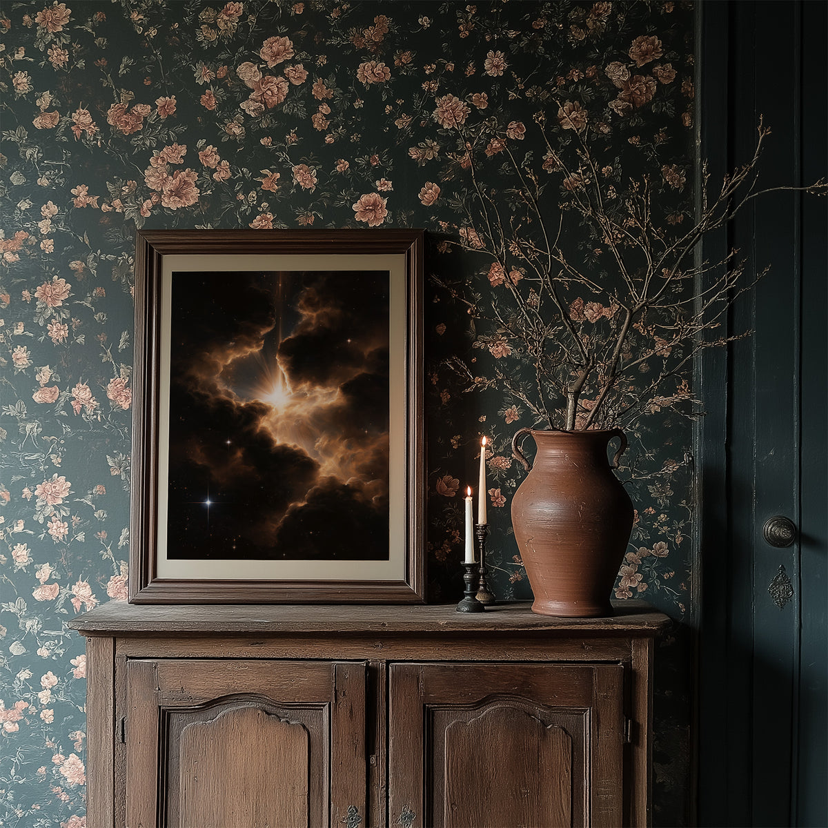 Embers Among the Cosmos, a nebula of gold and rust clouds glowing against a black sky dusted with small stars, painted in ember gold, umber and deep black, in a dark frame on a wooden dresser against floral wallpaper