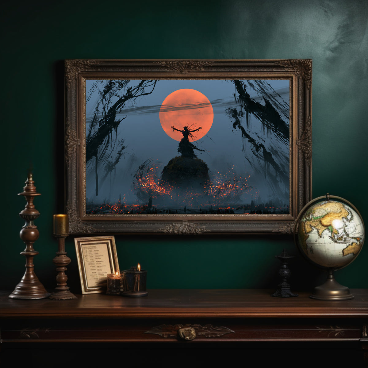 Embers at the Edge of Night, a dark witch silhouette on a hill before a huge orange moon, small fires glowing in the misty field below, in an ornate dark frame on a deep green wall above a mantel with a globe and candles