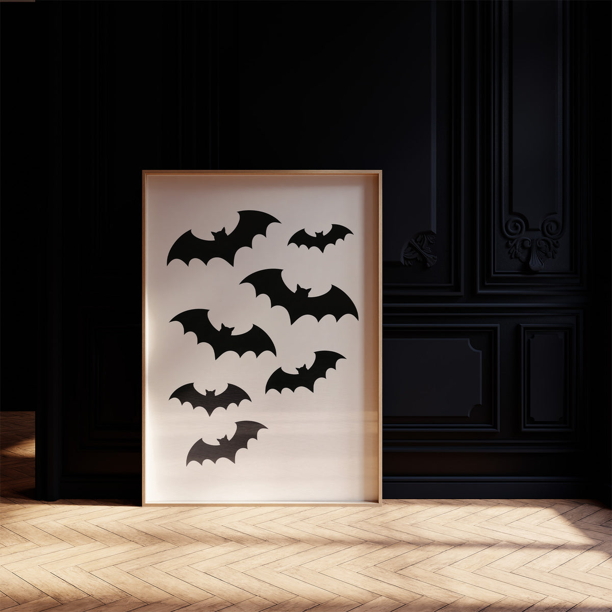 Evening Flight in Silhouette, a loose flock of black bat silhouettes spread across a cream ground in a simple, flat graphic arrangement, in a dark frame on a black paneled wall above a sunlit herringbone floor