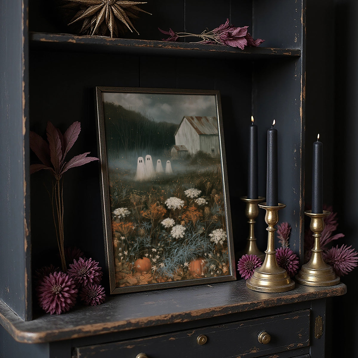 Fog Settles on the Low Field, a dark barn on a hill above a meadow of cream and rust wildflowers, a pale mist in the valley and two faint pale figures at the edge of the field, painted in forest green, rust and bone, in a dark frame on a black shelf beside brass candles and dried leaves