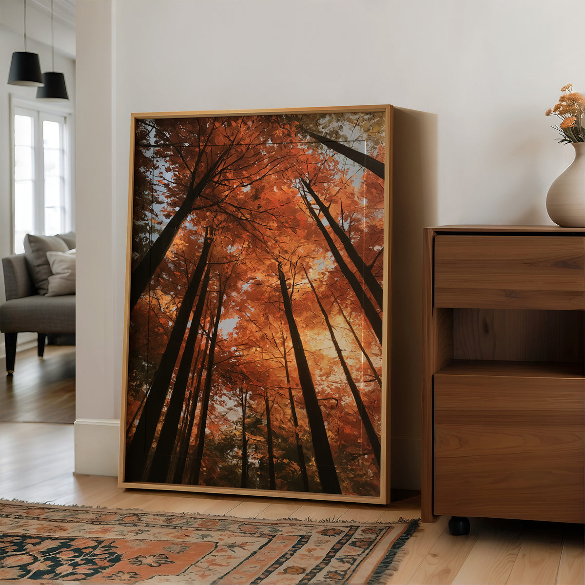 Look Up Into the Burning Wood, looking straight up through a canopy of tall dark trunks and orange autumn foliage, the pale sky glowing behind them, painted in rust, burnt orange and charcoal, in a wood frame on a wall beside a walnut cabinet and an open doorway