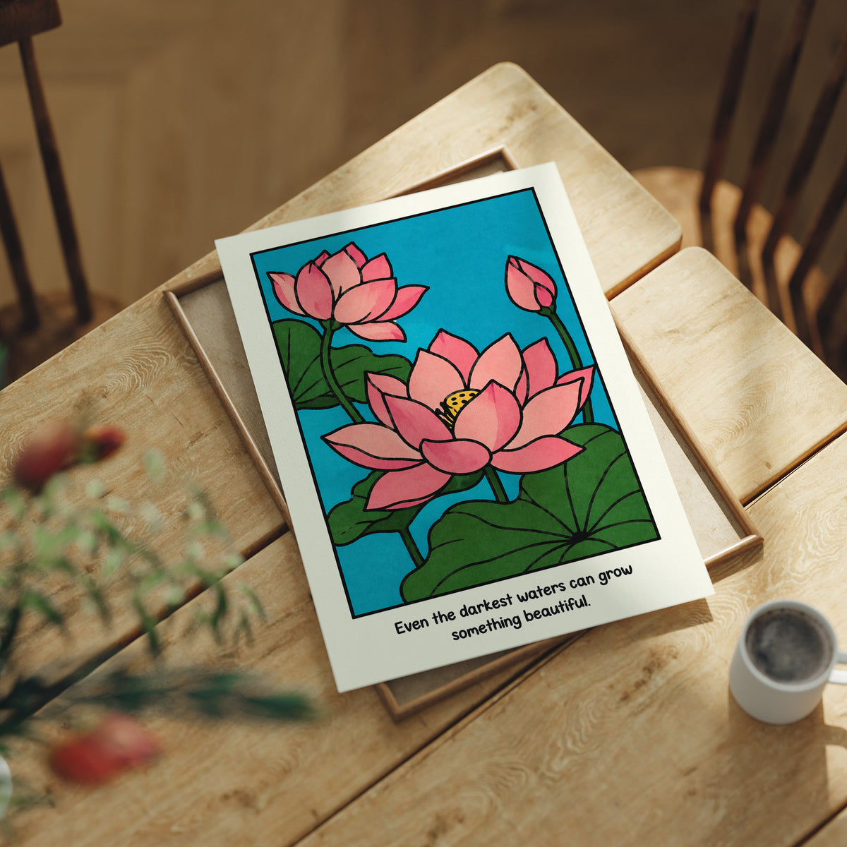 Lotus Rising From Dark Water, a pink lotus flower with a bud and large green leaves on a bright teal pond, with the quote Even the darkest waters can grow something beautiful in small black lettering along the bottom, lying flat on a light wood table beside a coffee cup and red berries