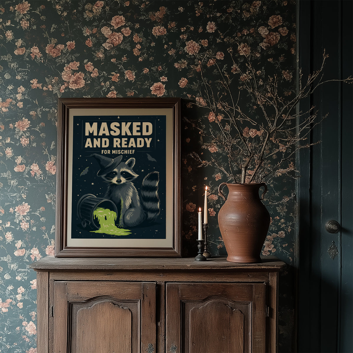 Mischief Wears a Mask, a masked raccoon beside a puddle of glowing green slime under bold cream lettering that reads masked and ready for mischief, in a dark frame on a wooden dresser against floral wallpaper