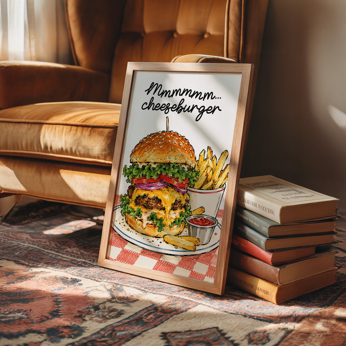 Mmmm Cheeseburger Makes Everything Better, a stacked cheeseburger with lettuce, tomato, cheese and a sesame bun beside fries and ketchup cups on a red and white checkered plate, with the lettering Mmmmm cheeseburger in black script across the top, in a wood frame on a rug beside a leather armchair and a stack of books