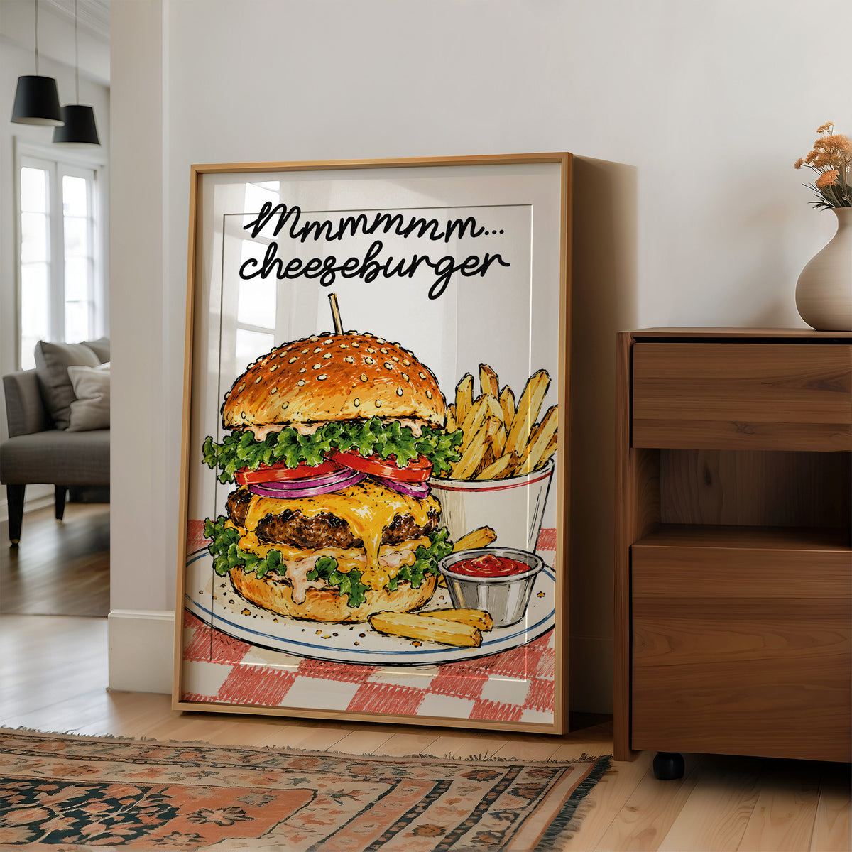 Mmmm Cheeseburger Makes Everything Better, a stacked cheeseburger with lettuce, tomato, cheese and a sesame bun beside fries and ketchup cups on a red and white checkered plate, with the lettering Mmmmm cheeseburger in black script across the top, in a wood frame on a wall beside a walnut cabinet and an open doorway