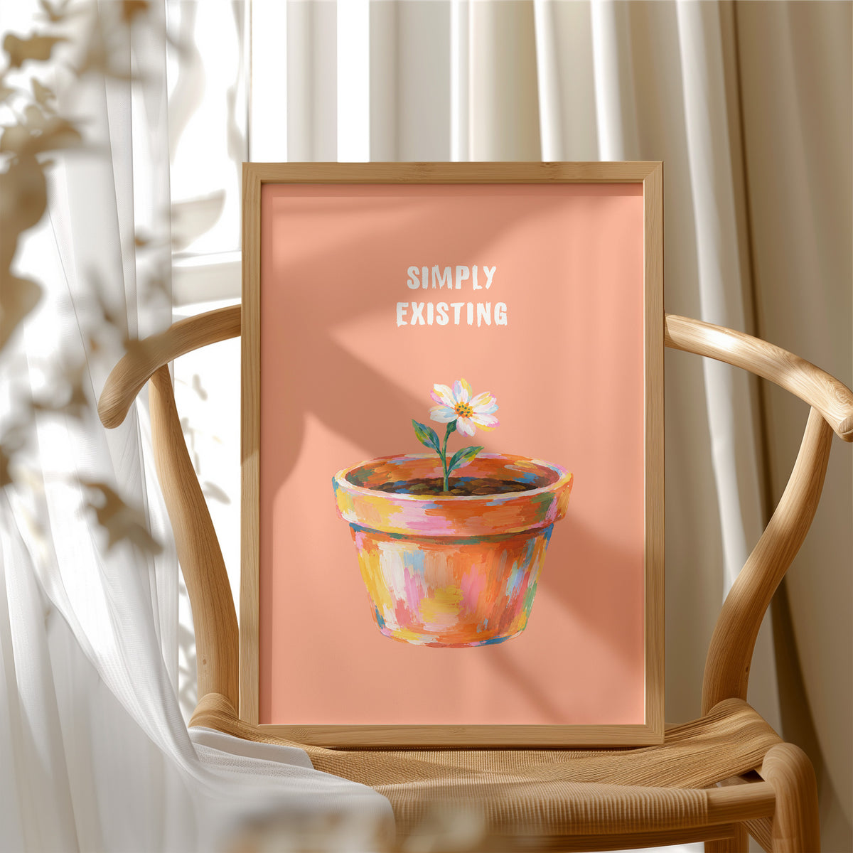 One Small Bloom in Clay, a single white flower rising from a painted clay pot in coral, gold and pink brushstrokes, on a peach ground with two lines of bold pale lettering above, in a loose painterly style, in a wood frame beside a wicker chair by a sunny window