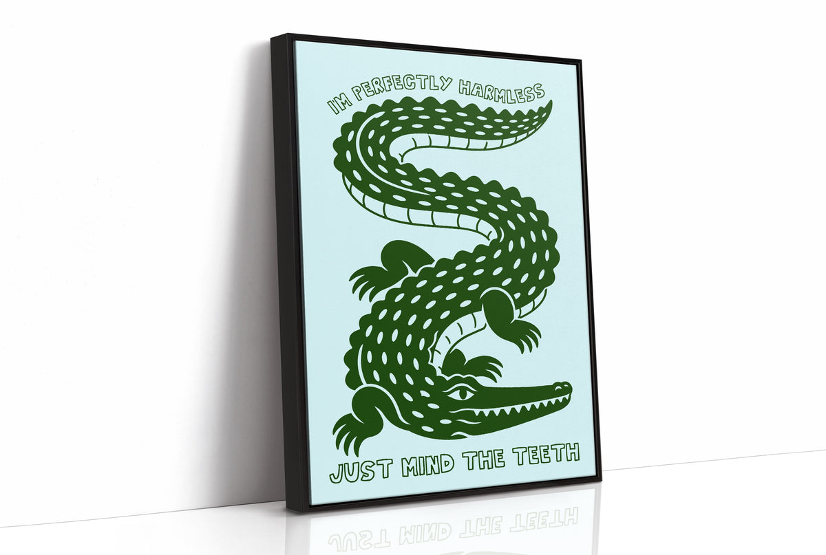 Perfectly Harmless, Mind the Teeth, a deep green crocodile curling down a pale mint ground, with a bold hand lettered line above reading I'M PERFECTLY HARMLESS and one below reading JUST MIND THE TEETH, as a framed canvas in a black frame