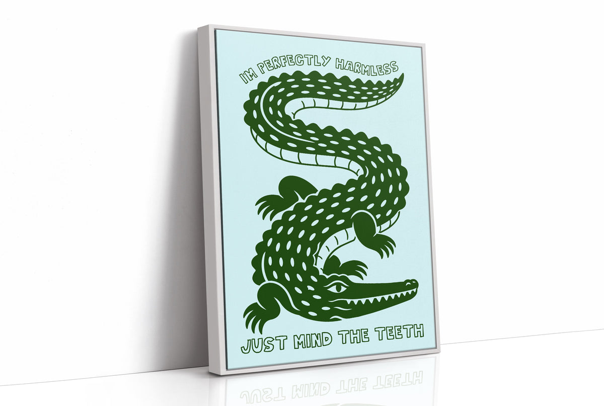 Perfectly Harmless, Mind the Teeth, a deep green crocodile curling down a pale mint ground, with a bold hand lettered line above reading I'M PERFECTLY HARMLESS and one below reading JUST MIND THE TEETH, as a framed canvas in a white frame