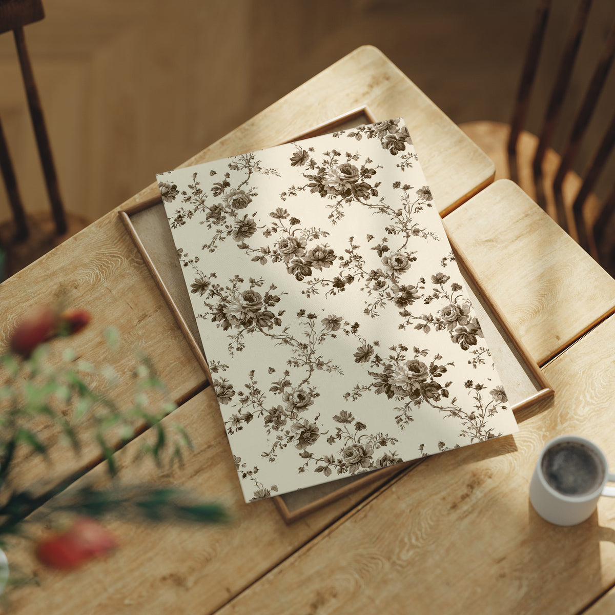 Roses Keep to the Linen, a repeating vintage pattern of brown roses and leafy sprigs on a cream ground, lying flat on a light wood table beside a coffee cup and red berries