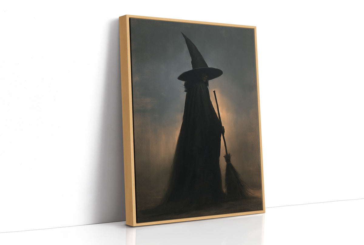 She Rides Out at Midnight, a witch in a tall pointed hat and long cloak, a broomstick at her side, a silhouette against a dusky amber and blue haze, as a framed canvas in a natural wood frame