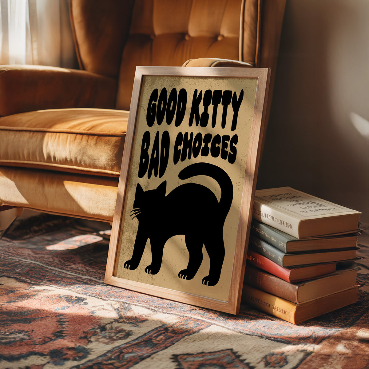Sleek Silhouette, Questionable Taste, a solid black cat silhouette with a long tail curled up the side, standing on tan paper with the words GOOD KITTY BAD CHOICES in bold black lettering, in a wood frame on a leather armchair beside a stack of books