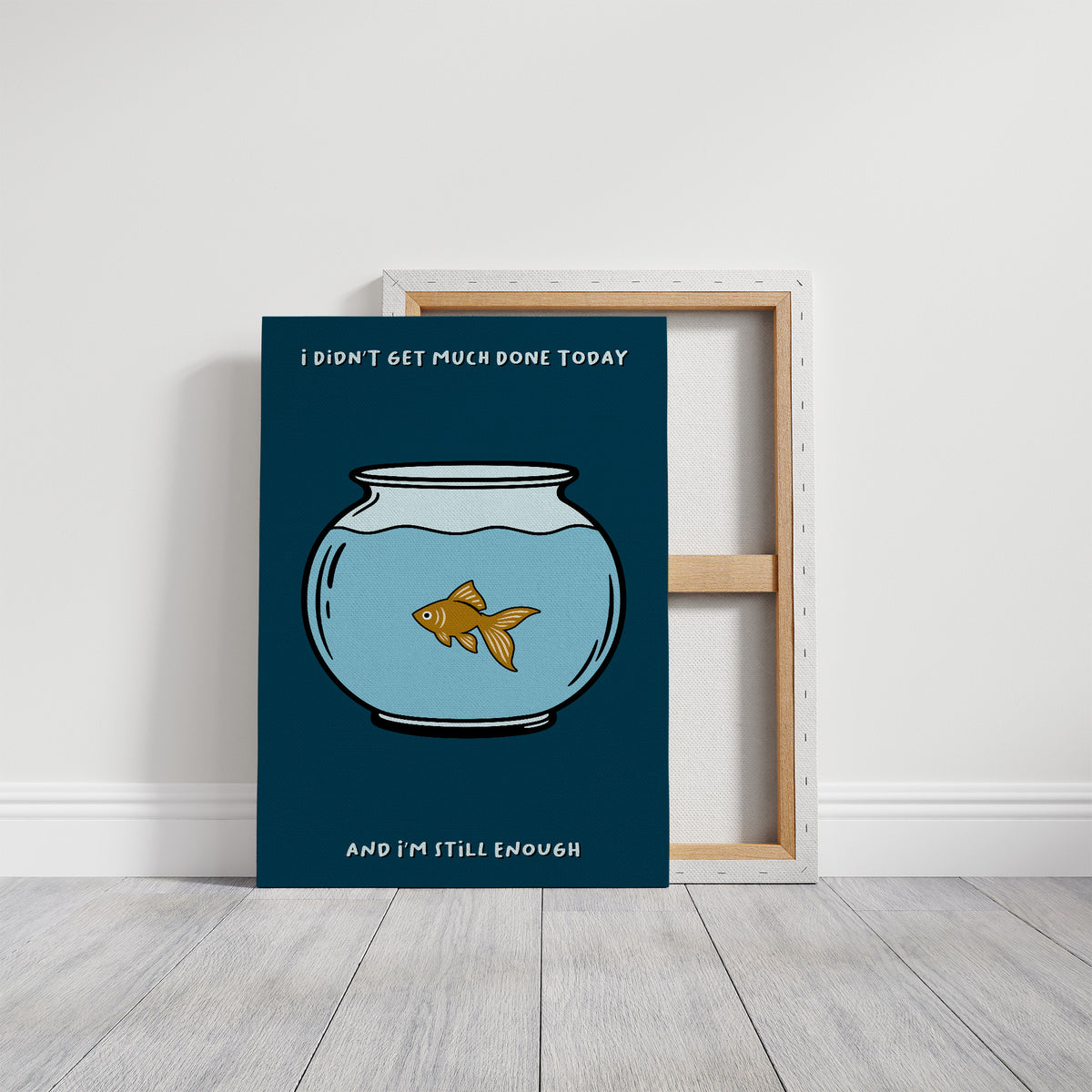 Still Enough for Today, a round glass fishbowl with one goldfish on a deep navy ground, a line of cream lettering above and below in a cartoon style, painted in navy, pale blue and orange, on a gallery canvas with wrapped edges leaning against a white wall