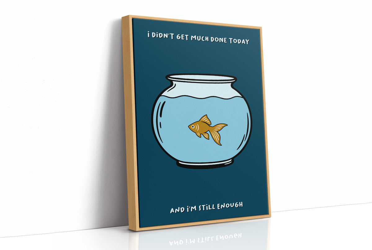 Still Enough for Today, a round glass fishbowl with one goldfish on a deep navy ground, a line of cream lettering above and below in a cartoon style, painted in navy, pale blue and orange, as a framed canvas in a natural wood frame