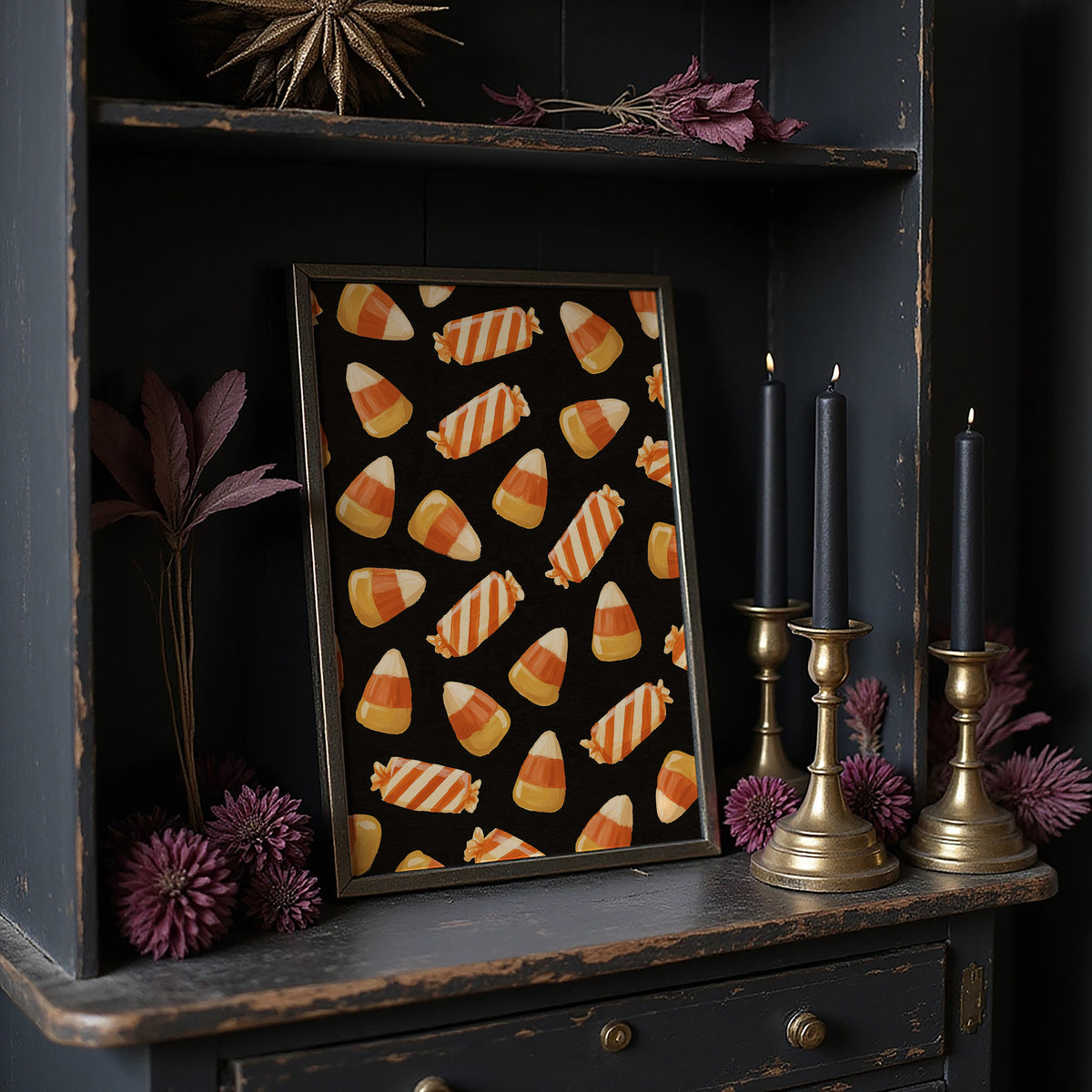 Stripes Kept for Later, a repeating pattern of candy corn kernels in cream, orange and butter yellow on a deep black ground, in a dark frame on a black shelf beside brass candles and dried leaves