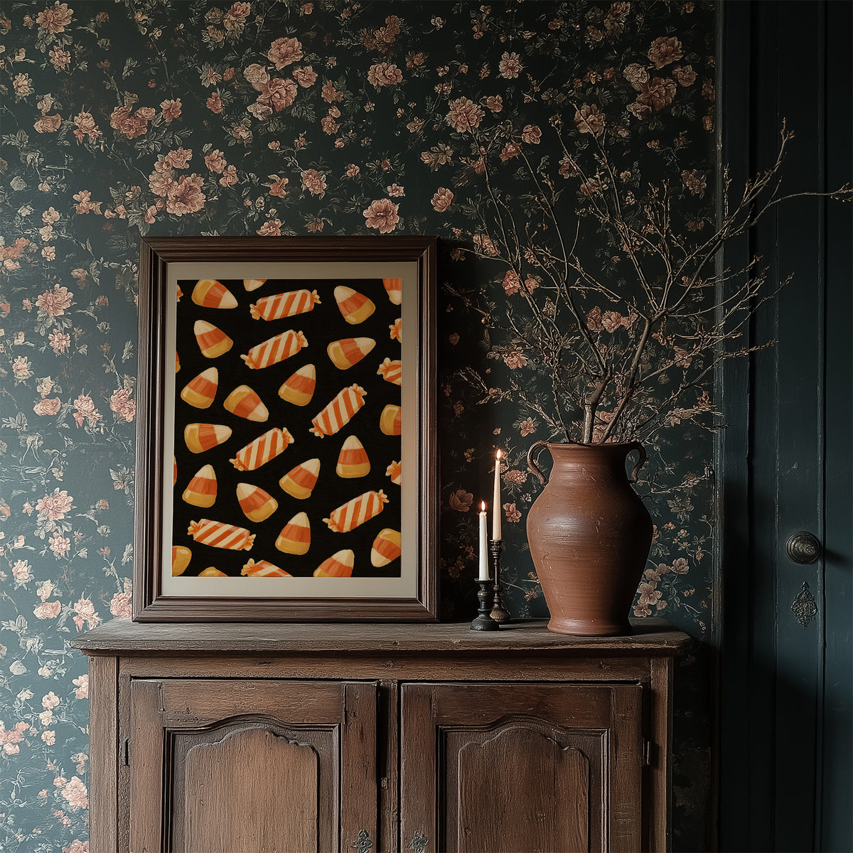 Stripes Kept for Later, a repeating pattern of candy corn kernels in cream, orange and butter yellow on a deep black ground, in a dark wood frame on a floral wallpaper wall above a rustic cabinet and a vase