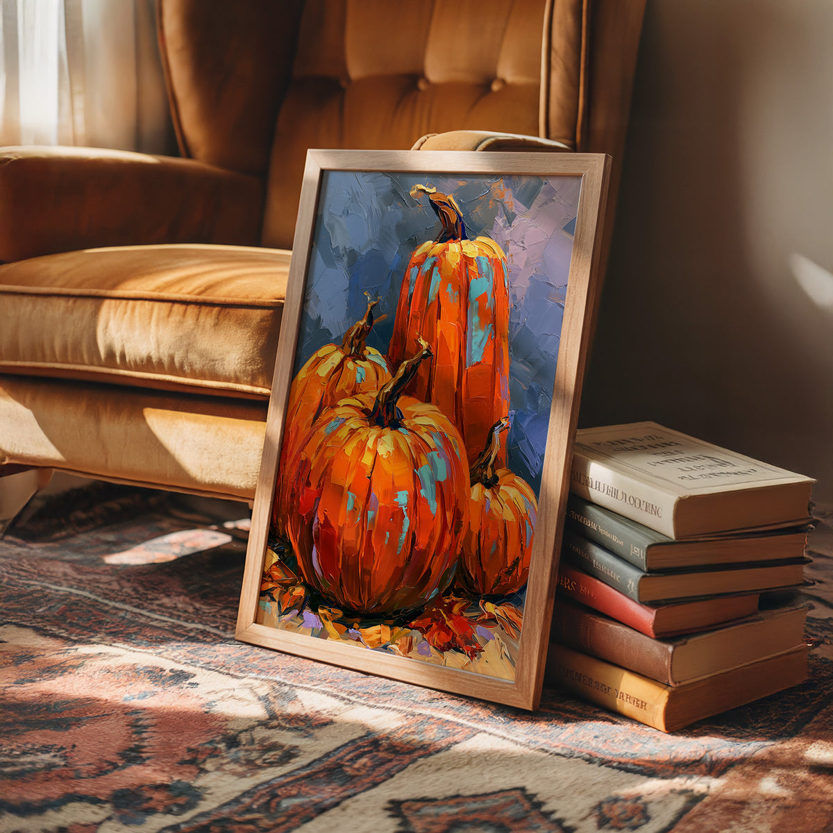 The Harvest Keeps Its Blue Hour, three painted pumpkins in orange and teal on a dusky blue ground with fallen leaves at their feet, in a loose, bold, painterly style, in a wood frame on a rug beside a leather armchair and a stack of books