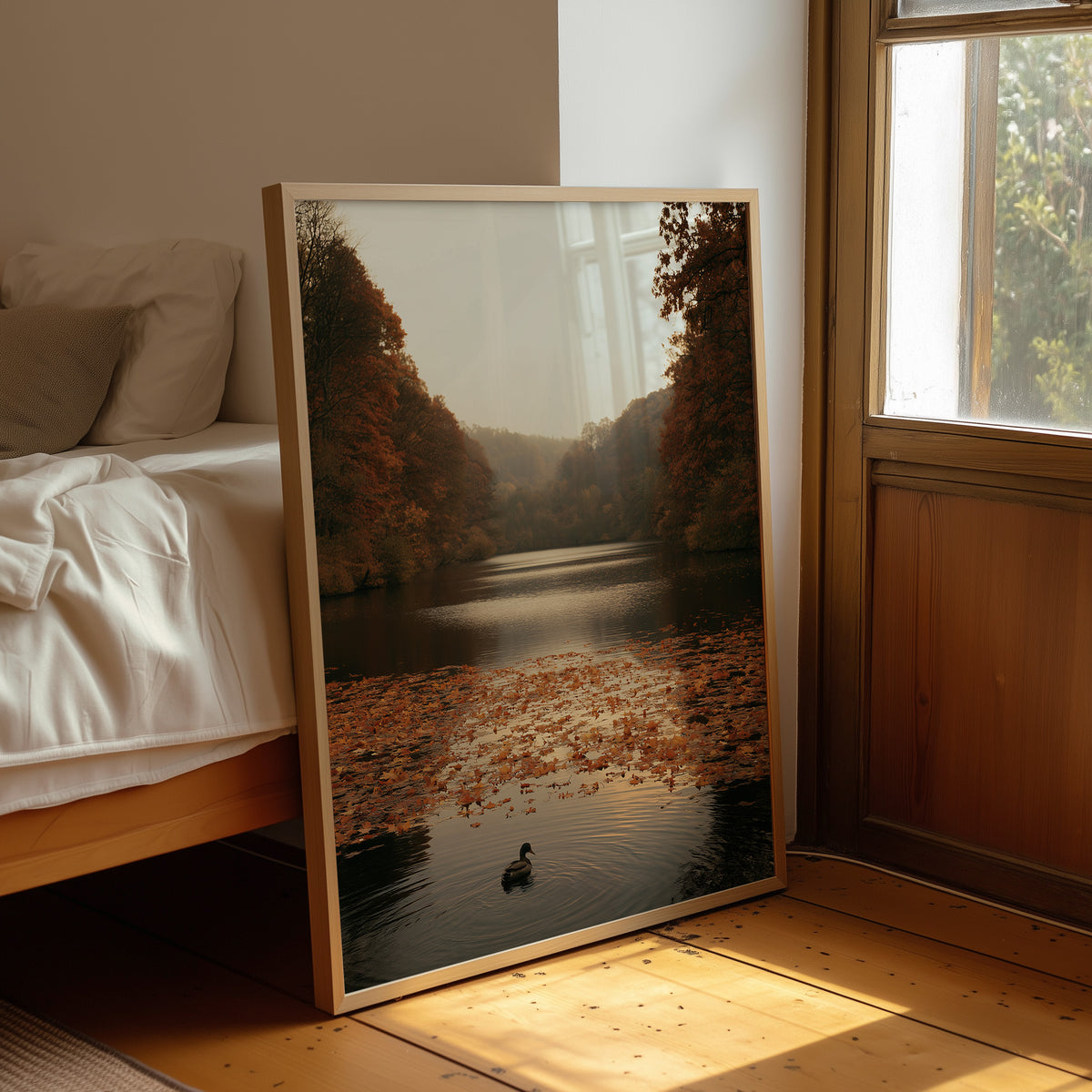 The Swan Waits on the Lake, a lone swan drifting on still water under turning autumn trees, with fallen leaves on the shore and a hazy golden light, painted in rust, amber and soft slate, leaning on a wood floor in a bedroom beside white linen bedding