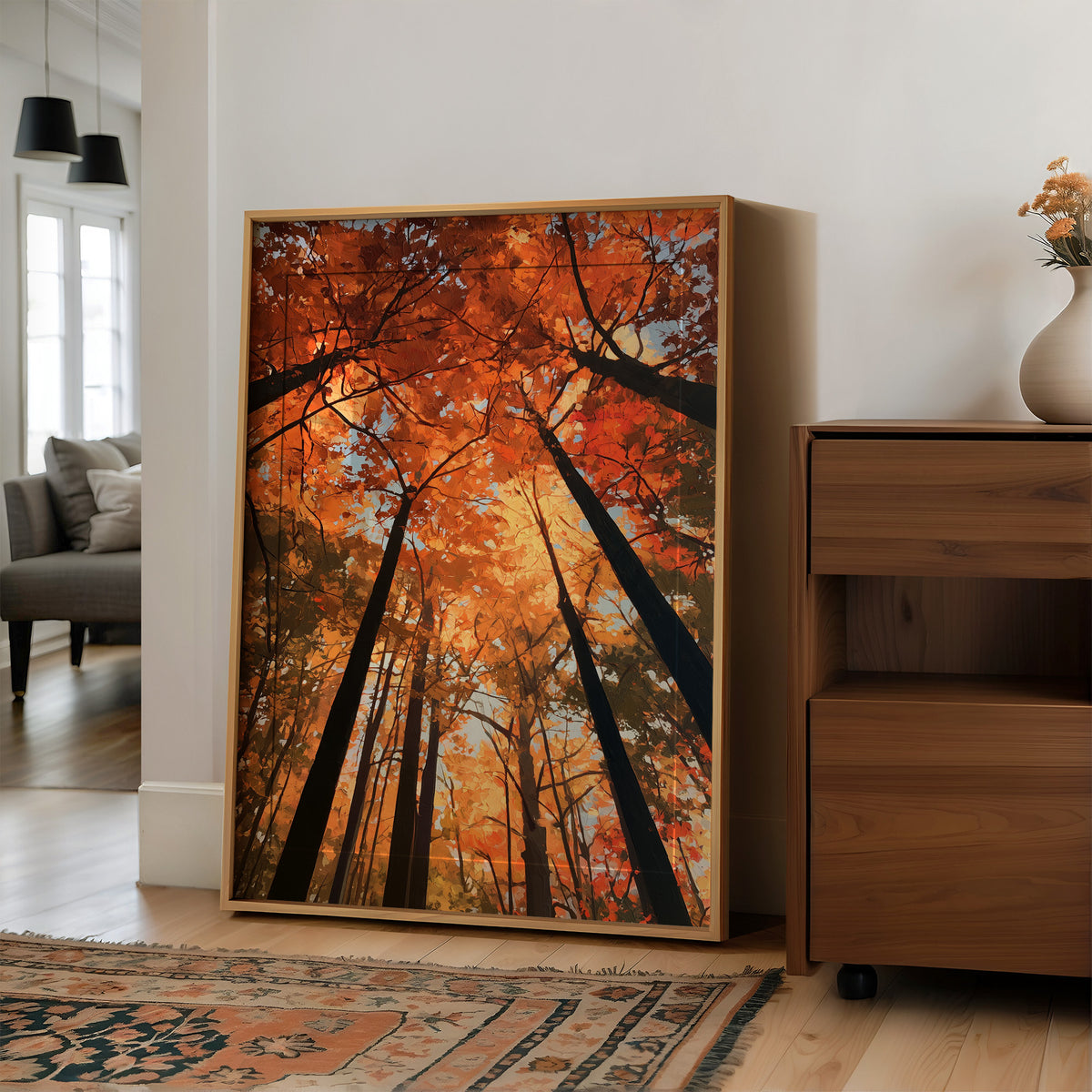 The Woods Blaze Overhead, a looking up view of tall trees with fiery red and orange autumn canopy and a sky of soft light, painted in flame red and burnt gold, in a wood frame on a wall beside a walnut cabinet and an open doorway