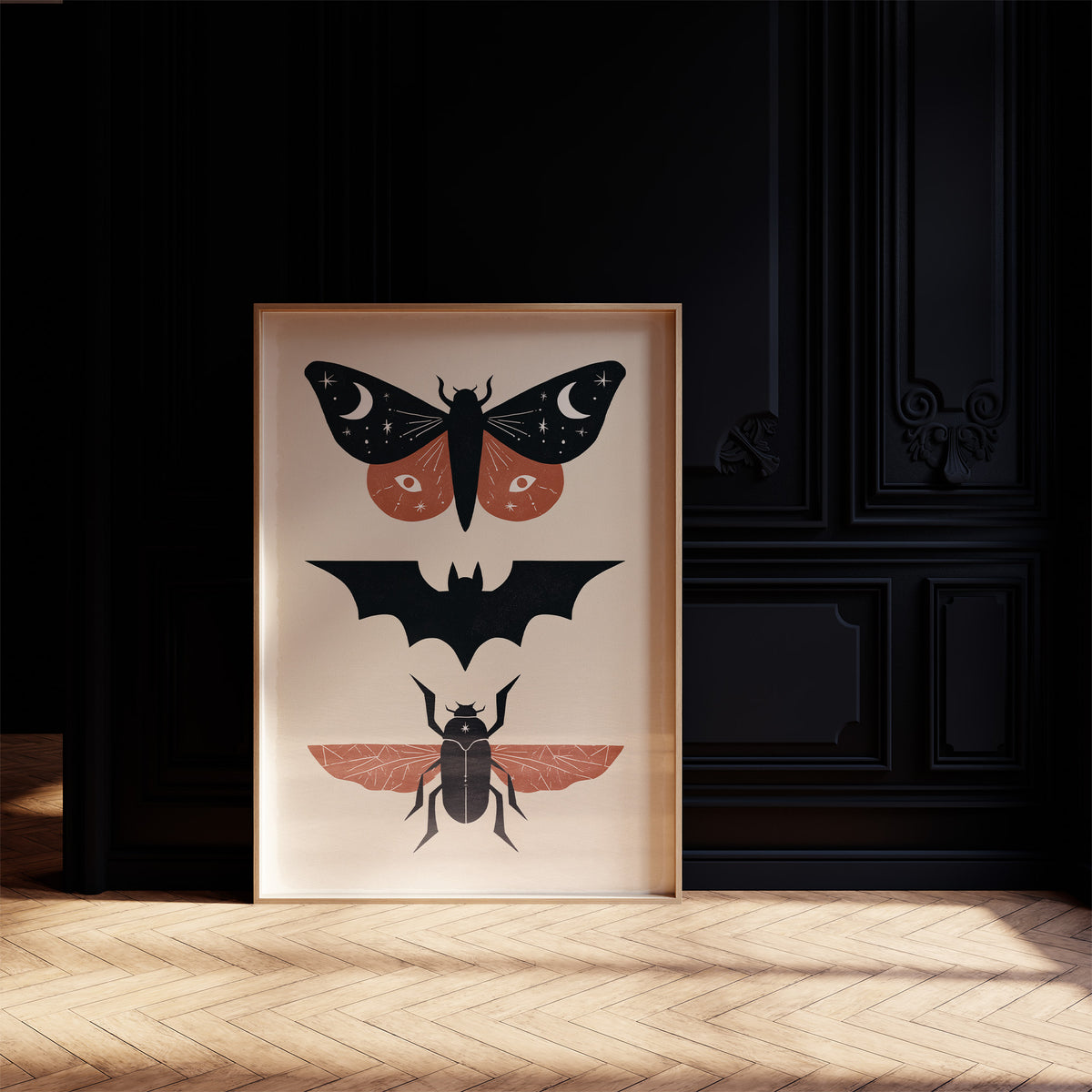 Three Night Visitors in a Row, a moth with crescent moon spots, a black bat in flight and a beetle with rust wings stacked in a column on a cream ground, painted in black, rust and cream, in a dark frame on a black paneled wall above a sunlit herringbone floor