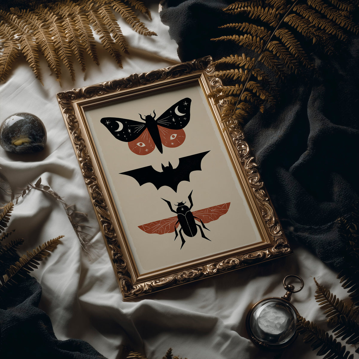 Three Night Visitors in a Row, a moth with crescent moon spots, a black bat in flight and a beetle with rust wings stacked in a column on a cream ground, painted in black, rust and cream, in an ornate frame on silk cloth beside ferns and a brass compass