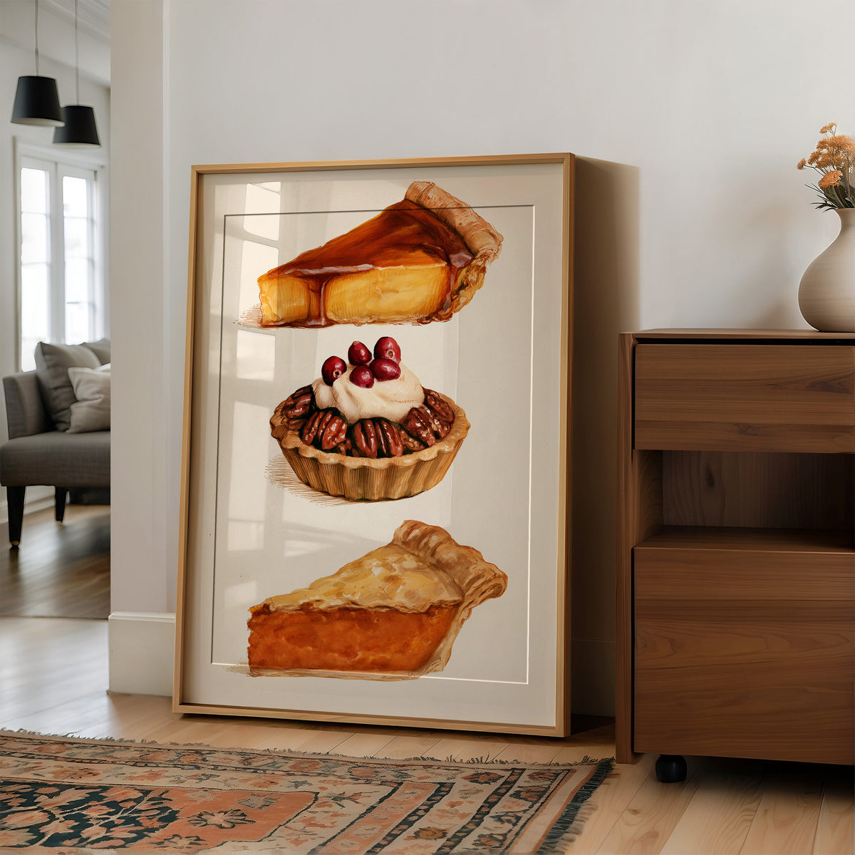 Three Slices Keep the Table Company, three pies stacked down the page, a golden custard slice, a pecan tart with cherries and a pumpkin wedge, on a cream ground, in a wood frame on a wall beside a walnut cabinet and an open doorway