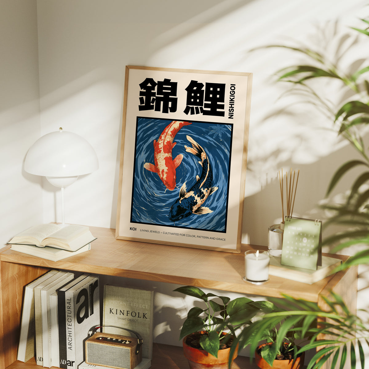 Two Fish Turn Beneath the Surface, two koi, one flame orange and one cream, turning through deep blue water with patient ripple lines, in a flat Japanese woodblock style, in a wood frame on a console table beside a white lamp and stacked books