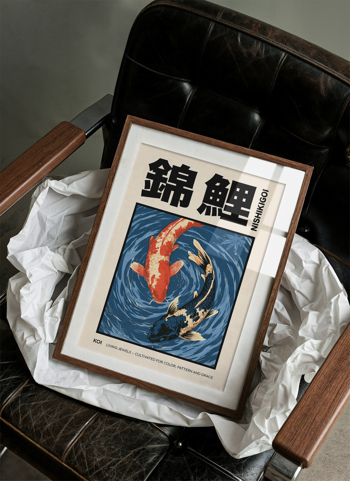 Two Fish Turn Beneath the Surface, two koi, one flame orange and one cream, turning through deep blue water with patient ripple lines, in a flat Japanese woodblock style, in a wood frame on a black leather armchair beside crumpled white tissue
