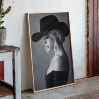 Framed portrait of a woman wearing a cowboy hat next to a potted cactus on a wooden shelf.