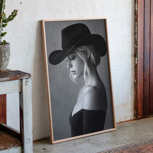 Framed portrait of a woman wearing a cowboy hat next to a potted cactus on a wooden shelf.