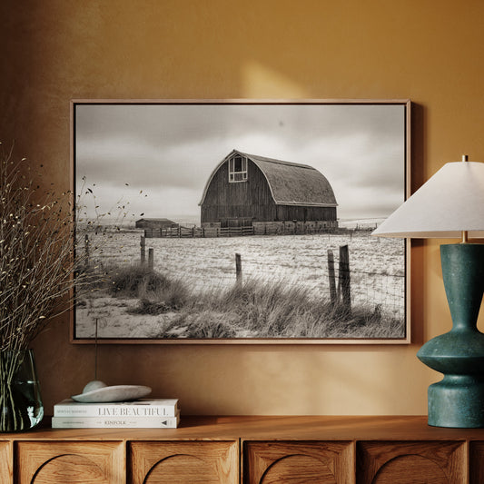 Framed black and white photo of a barn on a wall above a wooden cabinet with decor items.