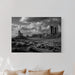 Black and white landscape print on a wall above a bed with beige pillows.