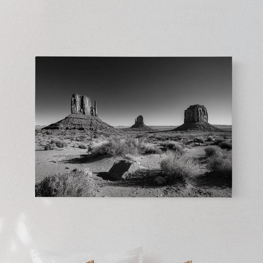 Desert landscape print on a wall above a bed with pillows and a lamp.