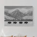 Bedroom with a mountain landscape print above a bed with beige pillows.