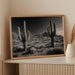 Framed black and white photograph of cacti on a shelf with decorative items.