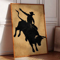 Framed artwork of a silhouette of a cowboy riding a bull on a wall.