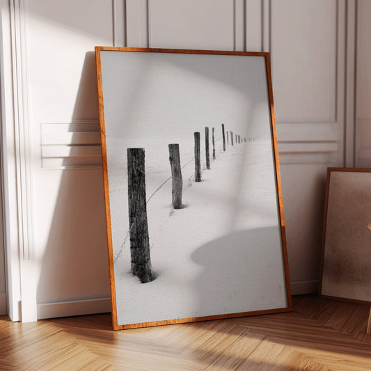 Framed photograph of a snowy landscape with wooden posts in a room with wooden floor and chair.