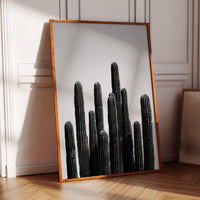 Framed black and white cactus print on a wall in a room with wooden floor and chair.