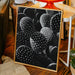 Framed artwork of cacti on a wooden floor with a chair and plants in the background